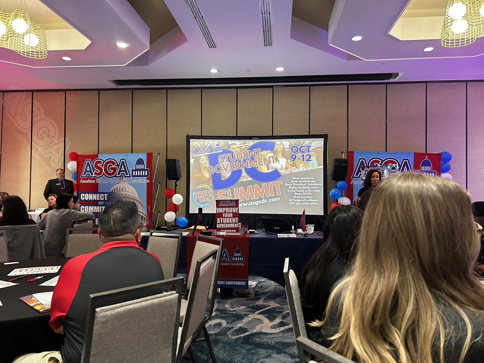 A hotel ballroom set up for an ASGA conference, seen from the audience: ASGA banners either side of a projection screen