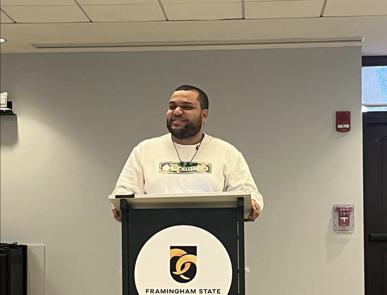 A speaker smiling at a podium that carries the Framingham State logo