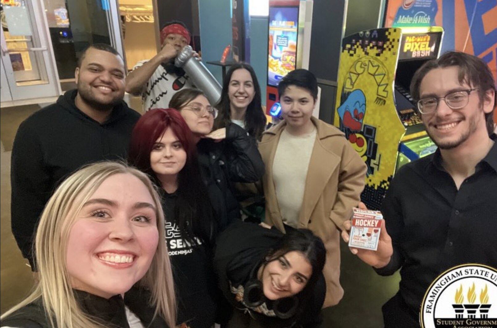 Eight Framingham State student government members crowd into a group selfie beside arcade machines